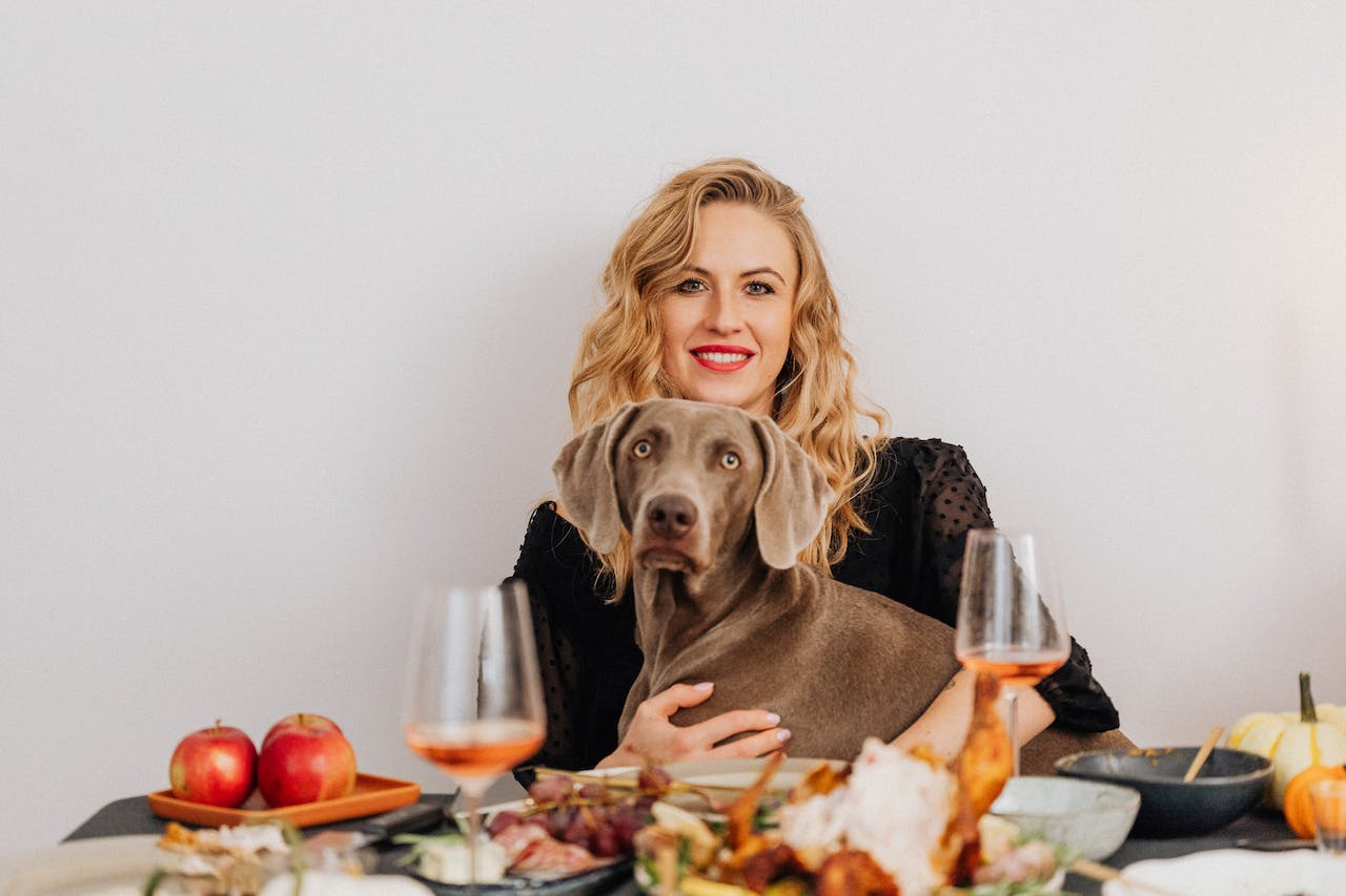 A woman sitting down with her dog having Thanksgiving dinner