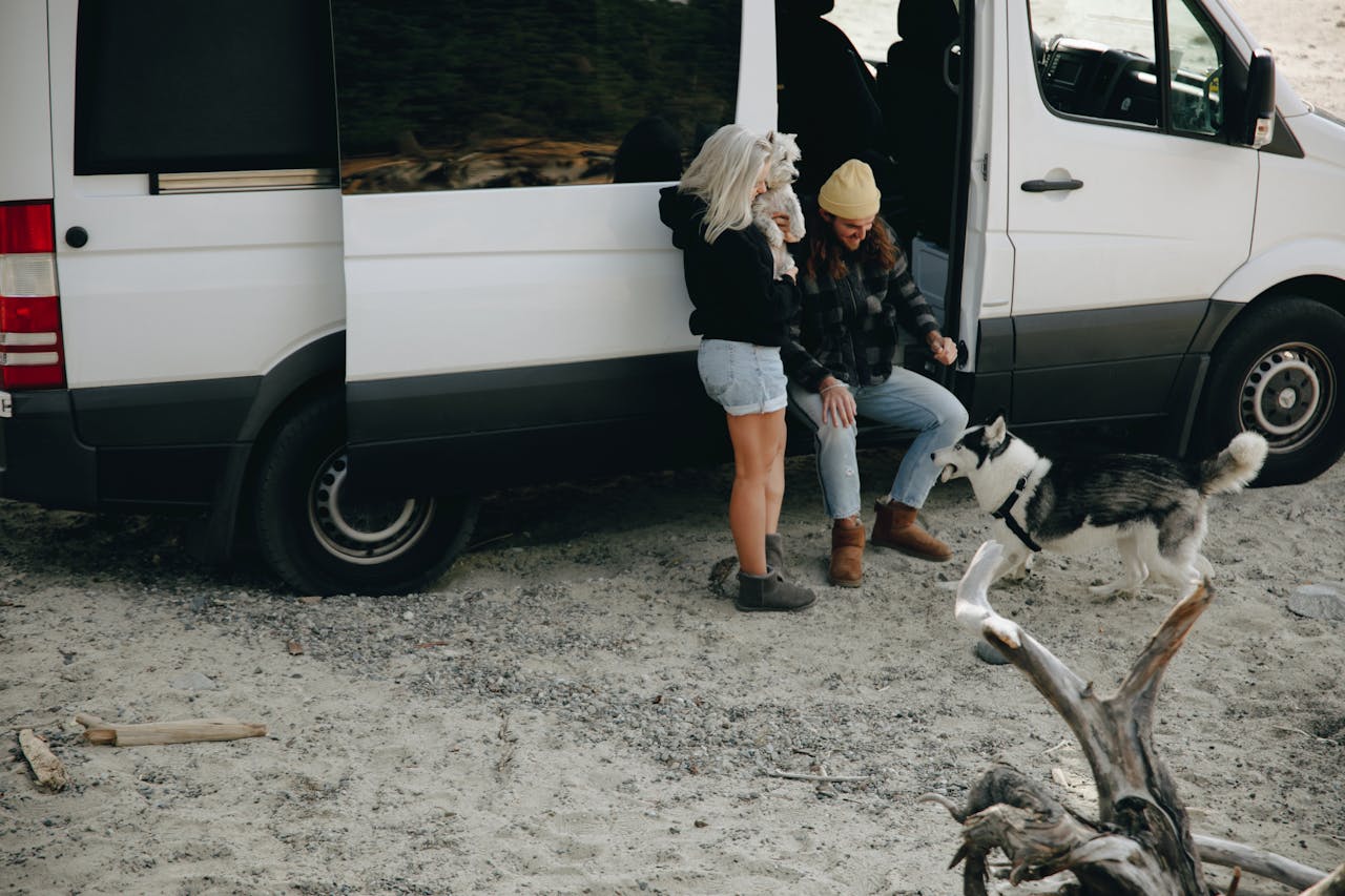 A couple sitting down next to an RV while their dog protects them